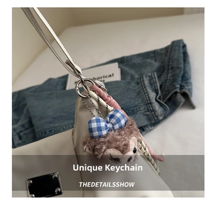 Detail eines Plüschfuchs-Anhängers mit blauer Schleife an einer weißen Ledertasche