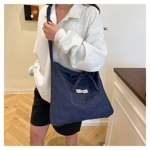 Close-up of blue denim tote bag featuring decorative bow drawstring and white fabric label
