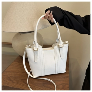 Détail du sac cabas en cuir blanc avec ferrures dorées sur une table en bois
