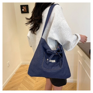 Detail of blue denim tote bag featuring side bow decoration and small white woven label