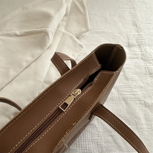 Brown leather tote bag with contrast white stitching and gold metal zipper detail