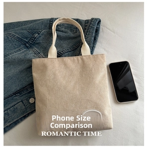 Detail view of corduroy tote bag texture and brand logo with smartphone for scale