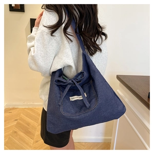 Close-up of deep blue denim tote bag with decorative bow and white letter patch