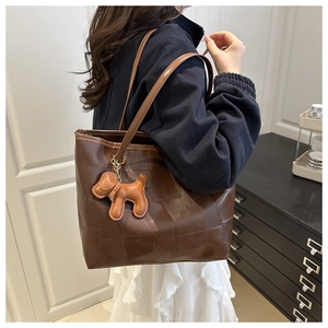 Detail of a large brown tote bag with patchwork texture and 3D dog charm on model shoulder
