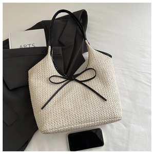 Detail of cream woven tote bag featuring black leather trim and elegant bow accent