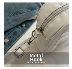 Detail of durable metal hook and zipper on a white PU leather bag with denim background