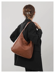 Detail view of large brown vintage hobo bag on shoulder against black blazer