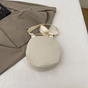 Minimalist beige round nylon crossbody bag with adjustable wide fabric strap on a flat lay