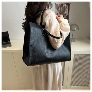 Black crocodile embossed tote bag worn as a shoulder bag in a modern office setting