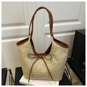 Detail of woven straw tote bag with brown leather trim and bow tie decoration