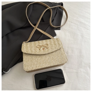 Straw crossbody bag detail showing woven texture with gold bow clasp and phone for scale