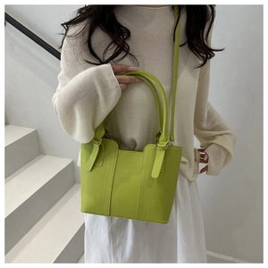 Détail du sac seau en cuir vert avocat avec anneau doré sur un escalier blanc moderne