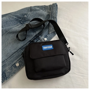 Detail of black nylon crossbody bag featuring blue logo tag and adjustable shoulder strap