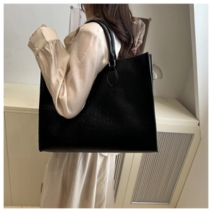 Close-up of a black tote bag featuring premium crocodile texture and slim shoulder straps