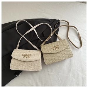 Detail of woven crossbody bag showing golden bow buckle and fine textured straw material