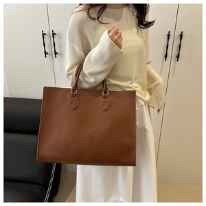 Detailed texture of brown crocodile pattern large tote bag held by a model in soft light