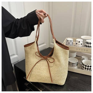 Close-up of beige woven tote bag with brown leather straps and a decorative bow detail