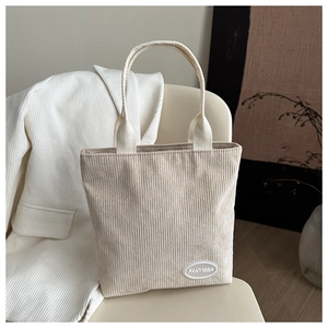 Detailed texture of cream corduroy tote bag featuring woven handles and brand label