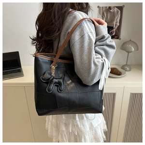 Détail d'un grand sac cabas noir en cuir avec bordure marron et pendentif chien mignon
