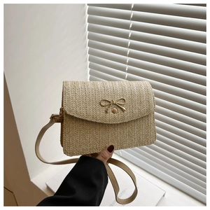 Detail of woven straw handbag featuring a decorative bow metal clasp and slim strap