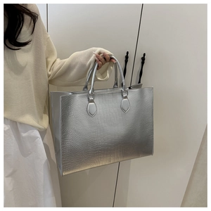 Detail of silver tote bag with crocodile pattern and metallic handles for daily commuting
