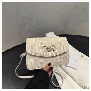 Macro detail of beige woven fishbone texture and golden bow ornament on a small bag