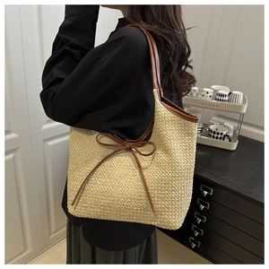 Detail of woven straw tote bag with brown leather trim worn over the shoulder by a model