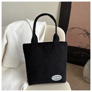 Detailed view of black corduroy tote bag with brand label on a soft light background
