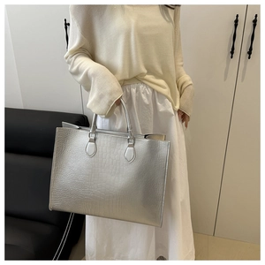 Detail of silver crocodile-embossed tote bag featuring dual handles and large capacity