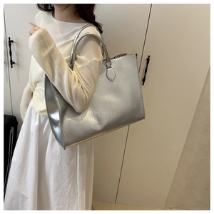 Close-up of a silver oversized tote bag with crocodile texture worn by a model