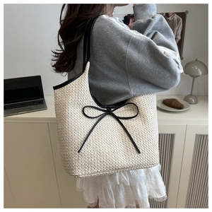 Detail of woven straw tote bag featuring black bow and leather straps on shoulder