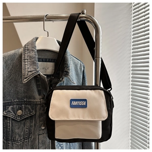 Detail of a casual black and white crossbody bag with a blue silicone brand logo and nylon strap