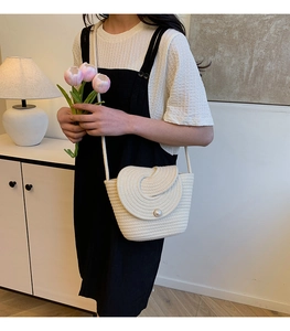 Detail of white woven crossbody bucket bag with pearl closure on a model