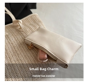 Detail of cream leather charm pouch with gold zipper on a woven straw tote bag