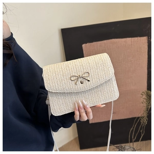 Detail view of woven cream shoulder bag with golden bow hardware and slim leather strap
