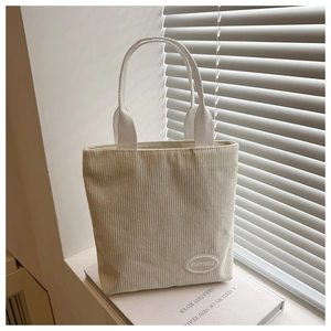 Detailed texture of white corduroy handbag with brand label on a soft light background