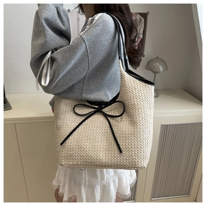 Close-up of woven straw tote bag featuring a black bow detail and faux leather straps