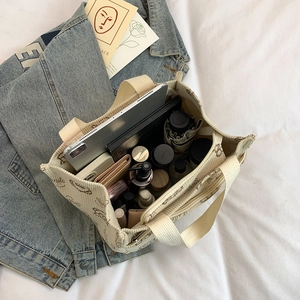 Borsa tote in velluto a coste con stampa smile contenente tablet e cosmetici su letto bianco