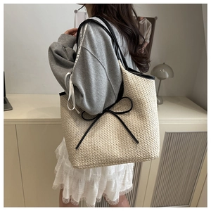 Detail of woven straw tote bag with black bow and shoulder straps on a female model