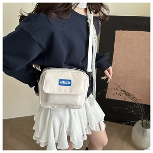 Detail of white nylon crossbody bag with blue brand label and adjustable shoulder strap