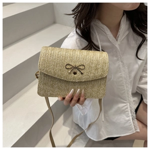 Detail of light beige straw crossbody bag featuring a golden bow-shaped metal buckle