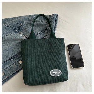 Detailed view of green corduroy tote bag showing vertical ribbed texture and brand label