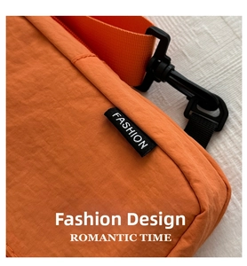 Detail of orange nylon crossbody bag with black FASHION tag and plastic buckle