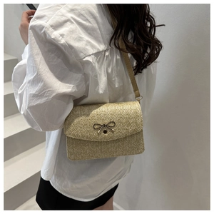 Détail du sac en paille beige clair avec un fermoir nœud doré sur un mannequin minimaliste