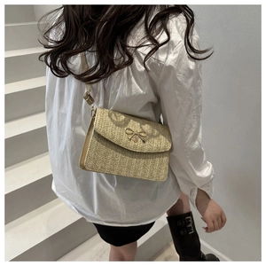 Close-up of woven straw shoulder bag with elegant gold metal bow and adjustable strap