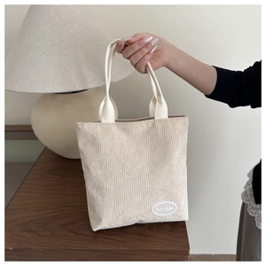 Detail of cream corduroy tote bag featuring reinforced handles and brand logo patch