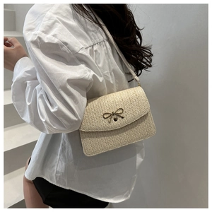 Detail shot of beige woven crossbody bag with a delicate golden metal bow clasp decoration