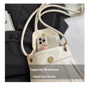 Internal capacity of off-white crossbody bag showing phone and cosmetics with tassel detail