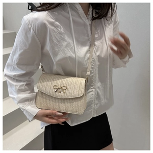 Detail of beige woven crossbody bag featuring a golden bow buckle and leather strap