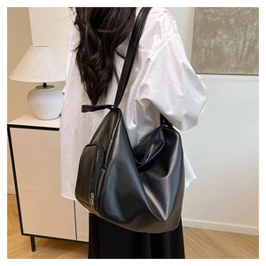Close-up of black PU tote bag showing side zipper pocket on a wide shoulder strap